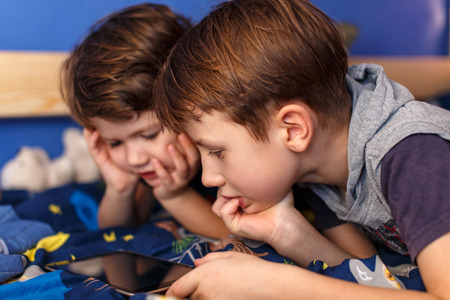 Little boys playing with tablet on the bed in the roomの写真素材