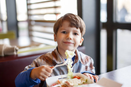 Little preschooler boy eating salad in fast food restaurantの写真素材