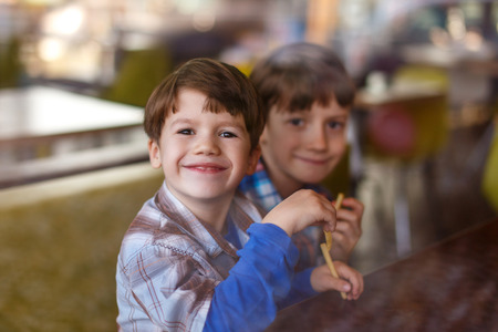 Little boys in fast food restaurant behind glass eating french friesの写真素材