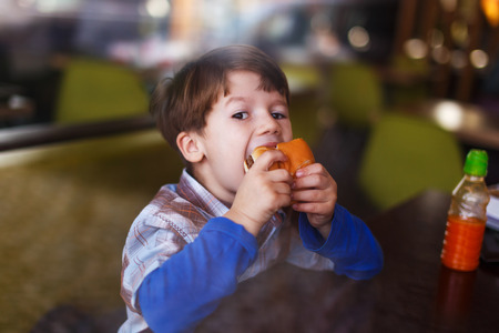 Little boy eat hamburger behind glass in fast food restaurantの写真素材