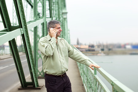 Successful businessman standing on bridge and calling outdoorの写真素材