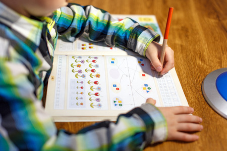 Little boy doing homework at home with pencil into maths workbook