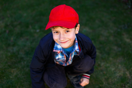 Little boy in red cap squat outdoor in meadowの写真素材