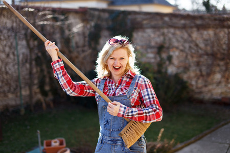 Crazy blonde woman playing with sweep like guitar, cleaning the backyardの写真素材