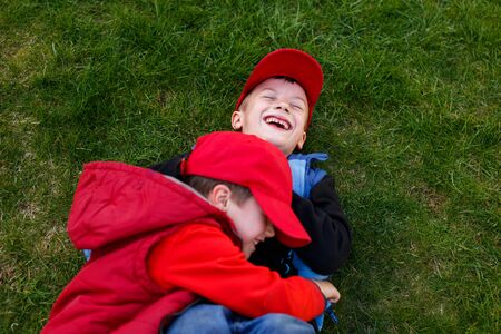 Little boys in cap on green grass laying and laughingの写真素材