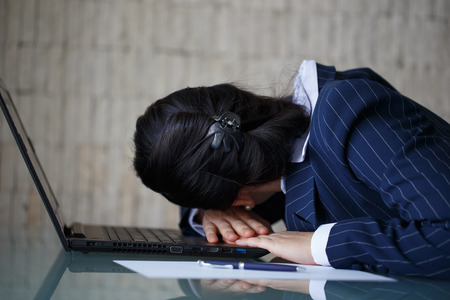 Tired businesswoman sleeping on laptop in officeの写真素材