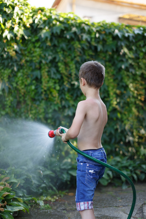 Little boy watering with hose outdoorの写真素材