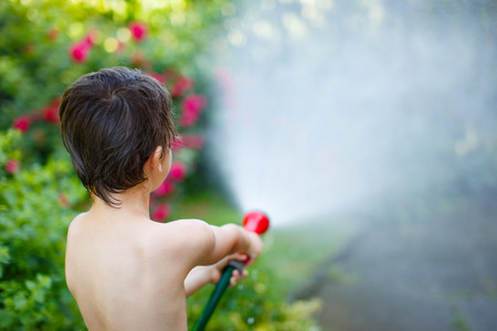 Little boy watering with hose outdoor closeupの写真素材
