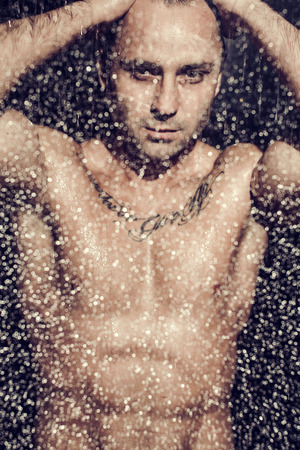 Sexy macho man posing under shower at nightの写真素材