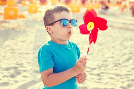 Little boy in sunglasses blowing pinwheel on beachの写真素材