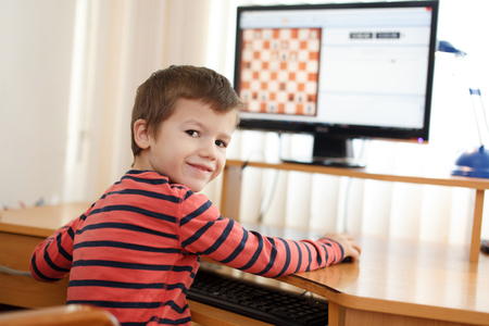 Little boy playing on PC chess looking back at homeの写真素材