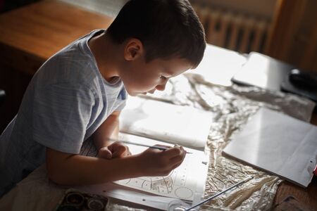 Little preschooler boy painting coloring book at home