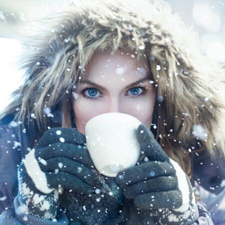 Winter woman drink from white mug in snowfallの写真素材