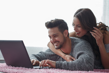 Happy couple prone on carpet online shopping indoorの写真素材