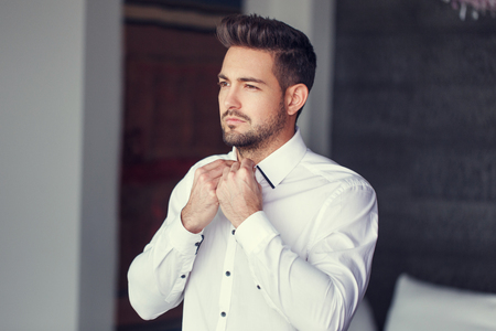 Young caucasian man dressing, put on shirt indoorの写真素材