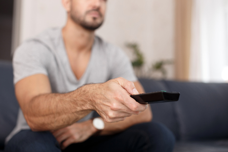 Man chaning TV channel by remote control at homeの写真素材