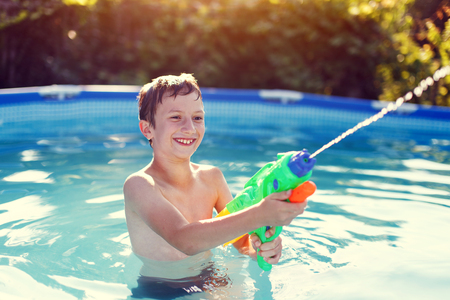 Happy little boy laugh and shoot with squirt gun in sunsetの写真素材