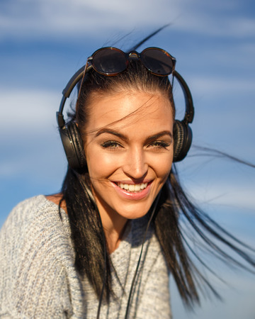 Young woman with headphones listening music outdoor, teeth smileの写真素材