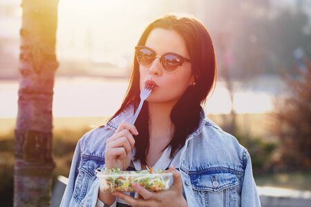Young woman with fresh salad and outdoor, fork in mouthの写真素材