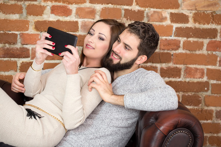 Young couple with tablet on sofa indoorの写真素材