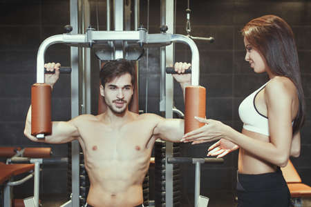 Man working out on chest machine in gym with personal trainerの写真素材