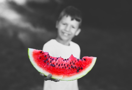 Little boy holding slice of watermelon outdoor, depth of field, selective colored black and whiteの写真素材