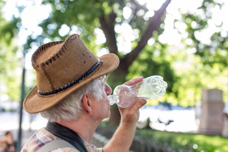 Senior thirsty tourist man drinking water from bottle in parkの写真素材