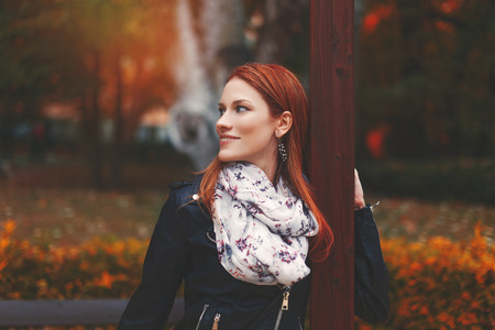 Young trendy redhead woman looking away in park at autumnの写真素材