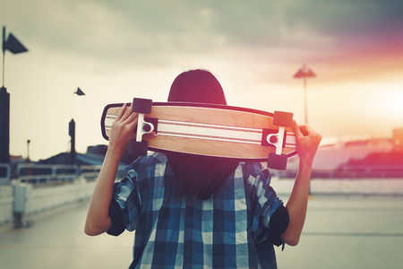 Young hipster woman holding skateboard behind head in sunset, outdoors, cinematic style, color gradedの写真素材