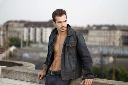 Sexy trendy muscular man with abs in denim posing outdoors in cityの写真素材