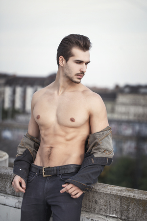 Young sexy muscular man in denim undress jacket outdoor, urban fashionの写真素材