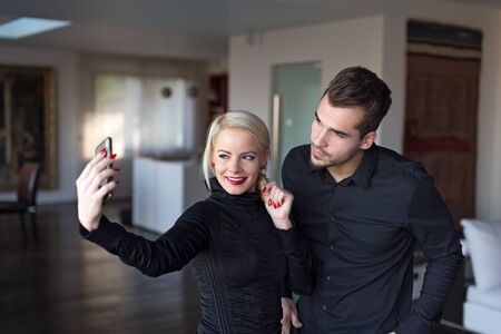 Happy young stylish couple in black outfit taking selfie indoor