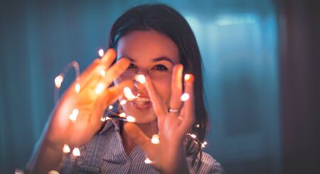 Young caucasian showing with LED fairy lights at home, playing with handsの写真素材