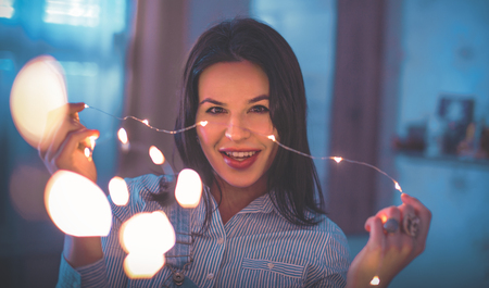 Young woman holding LED fairy lights indoors, smile at homeの写真素材