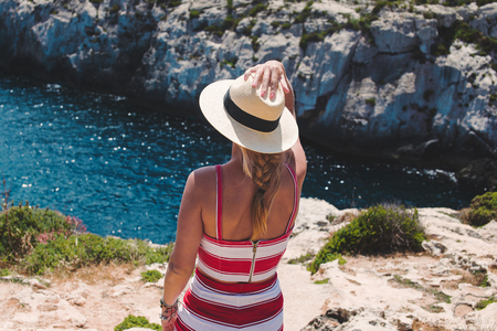 Woman in hat delighting in mediterranean scenery back view, Maltaの写真素材