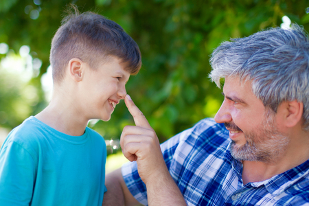 Father pushing sons nose in park, lie detectionの写真素材