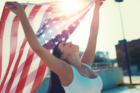 Happy young woman holding USA flag in air over headの写真素材