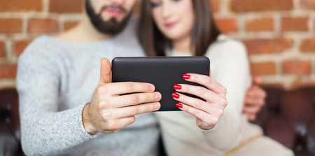 Young casual caucasian couple holding tablet together at home, closeupの写真素材