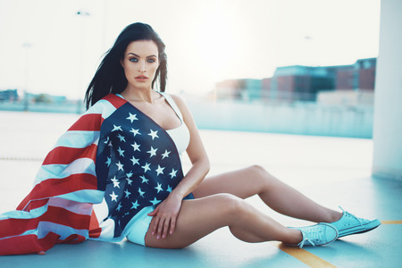 Sexy woman covered by USA flag sitting outdoors in sunlight