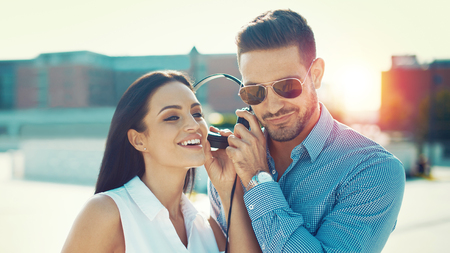 Happy young couple listening music in city, sharing headphones, outdoorsの写真素材