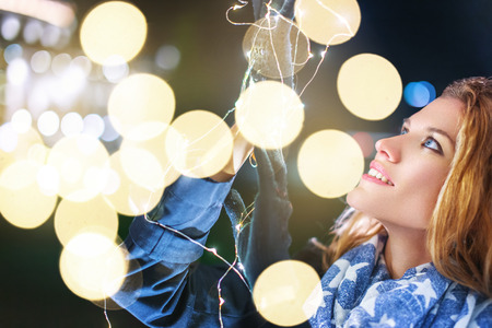 Young woman holding christmas fairy lights at night outdoors in city closeupの写真素材