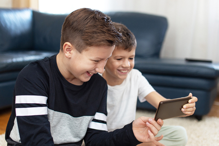 Happy boys using smartphone at home and laughing at homeの写真素材