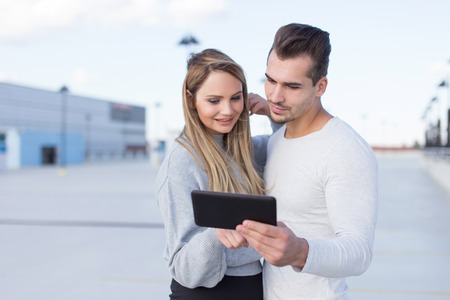 Happy young casual caucasian couple using tablet outdoors, online shopping