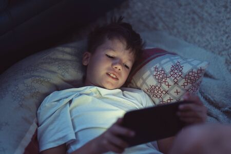 Little boy playing on digital tablet at night in bedroomの写真素材
