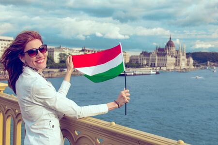 Happy young redhead hungarian urban woman stretching hungarian flag at Budapestの写真素材