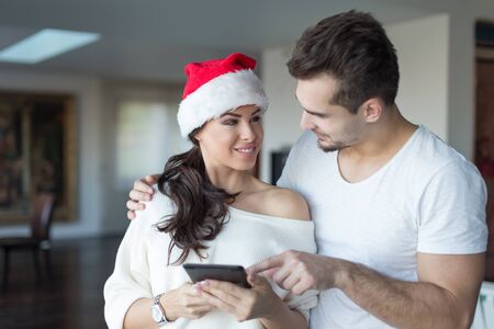 Happy young couple online shopping for Christmas on digital tablet at home, looking at each otherの写真素材