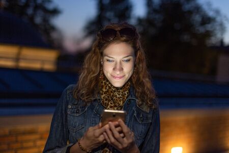 Young redhead urban woman reading message at evening outdoors
