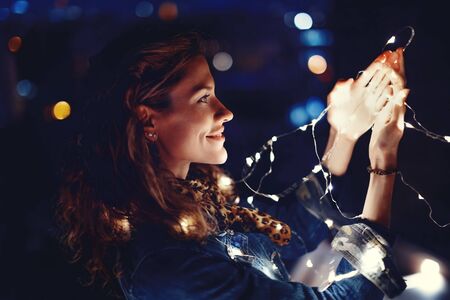 Young redhead Caucasian woman playing with fairy lights outdoors in dark