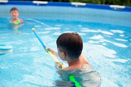 Happy young boys playing with water cannon in swimming pool at summer