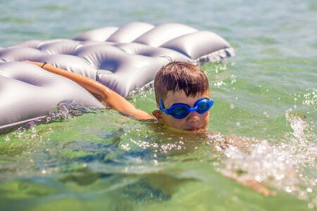 Happy little boy holding air water mattress in sea, summer holidayの写真素材